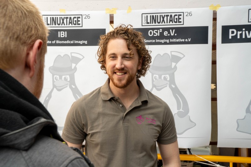 A person in a grey shirt with the private.coffee logo smiling at another person while talking about private.coffee